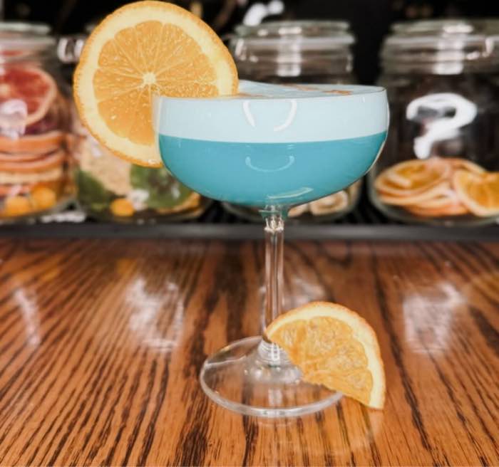 A pale blue coupe cocktail with a dried orange wheel