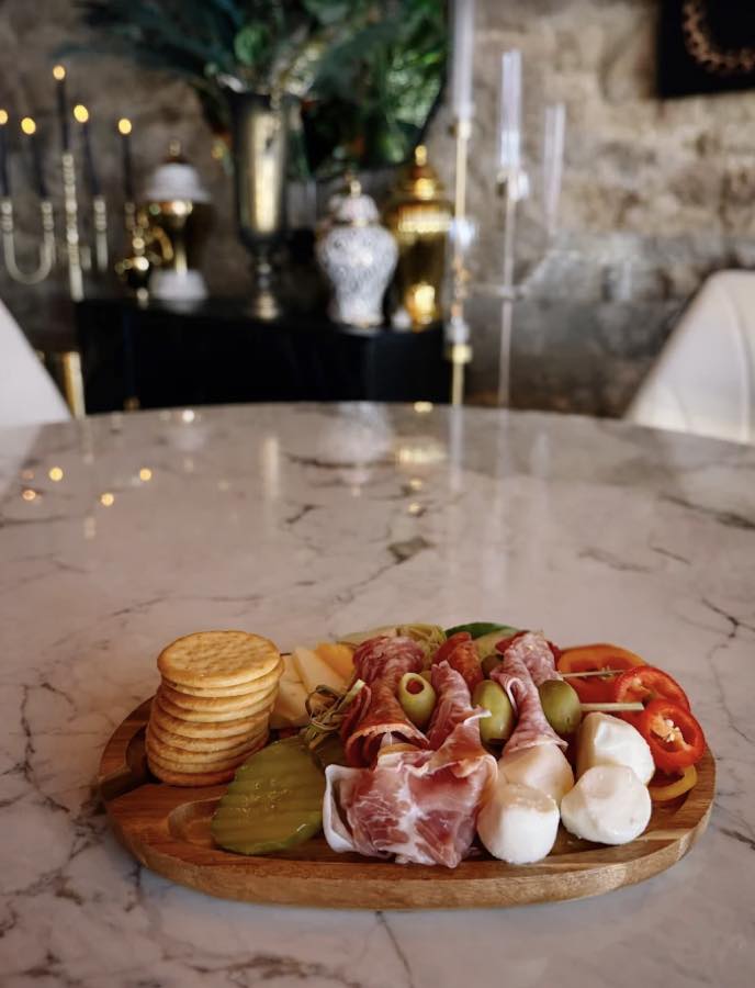A charcuterie board with cured meats, cheese and olives beside a glass of white wine
