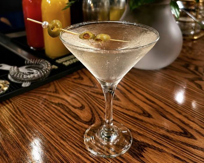 A martini with three olives on the wooden bar top