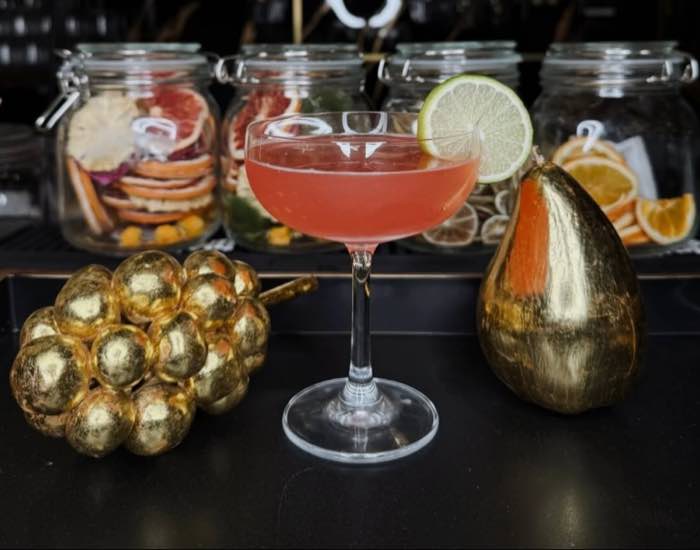 A pink coupe cocktail with a lime wheel and gilded fruit